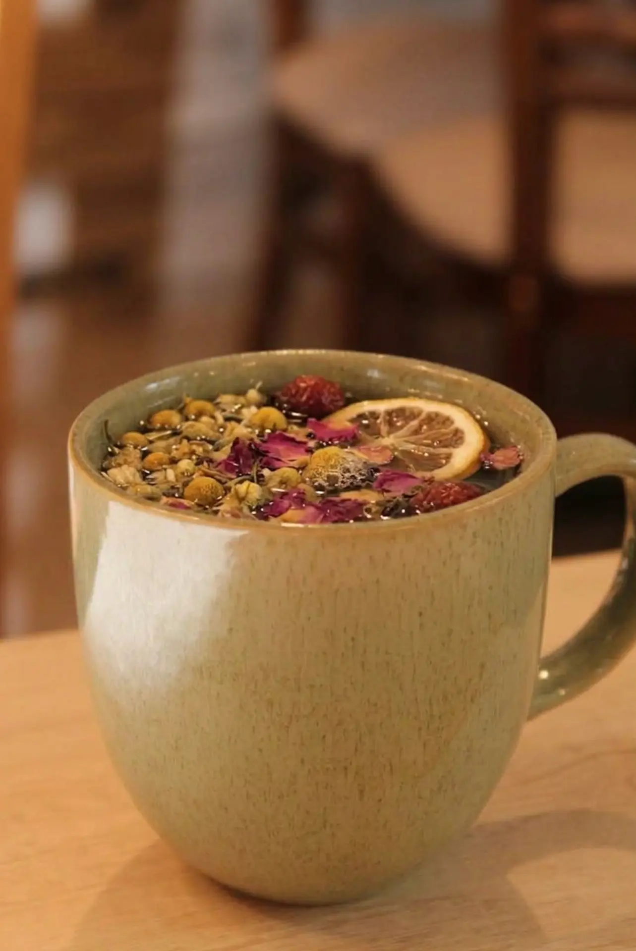 Tisana con manzanilla, pétalos de rosa, frutos rojos y rodaja de naranja en taza verde jade
